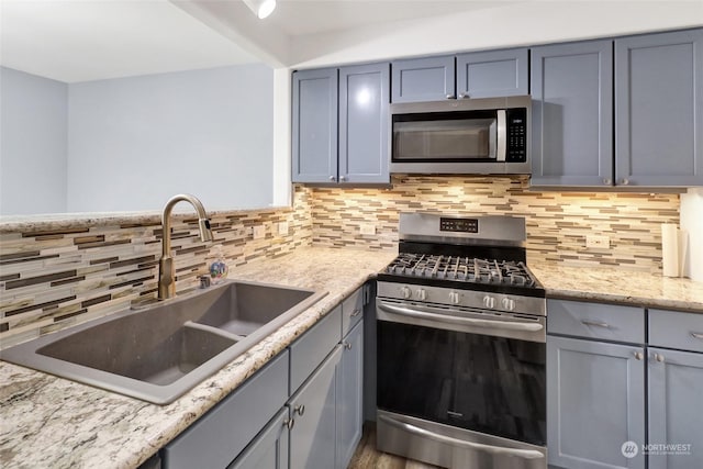 kitchen featuring decorative backsplash, sink, light stone counters, and stainless steel appliances