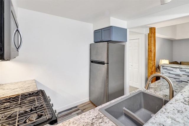 kitchen featuring hardwood / wood-style flooring, appliances with stainless steel finishes, light stone counters, and sink