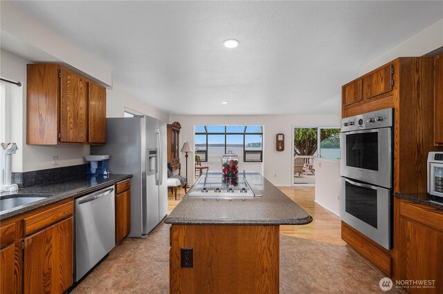 4030 Kamilche Point Rd, Shelton, WA 98584 - kitchen with appliances with stainless steel finishes, a kitchen island, brown cabinetry, recessed lighting, and dark stone countertops