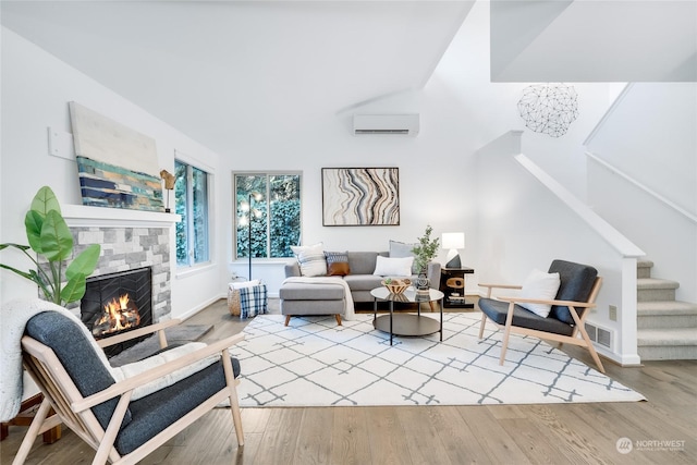 living room featuring a wall mounted air conditioner, light hardwood / wood-style flooring, a fireplace, and lofted ceiling