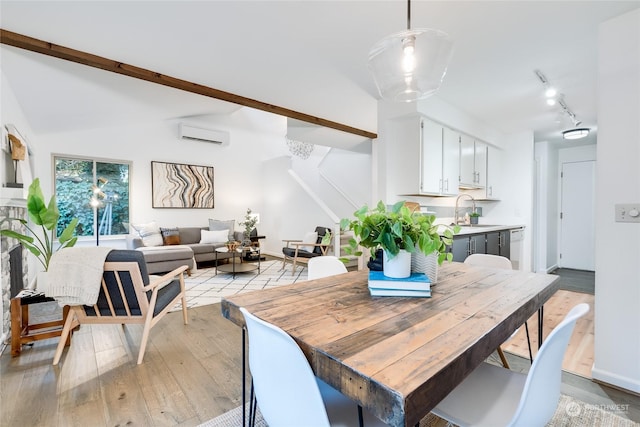 dining space with light hardwood / wood-style floors, an AC wall unit, sink, track lighting, and lofted ceiling with beams