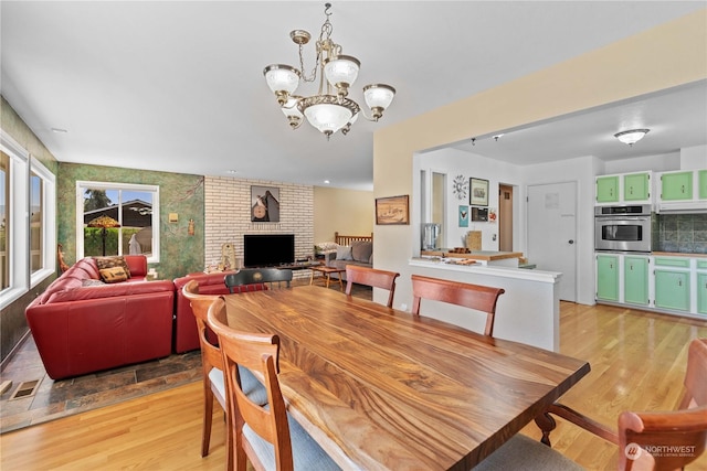 dining area featuring a brick fireplace, a chandelier, and light wood-type flooring