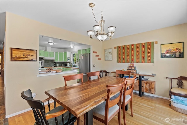 dining area with light wood-type flooring, a notable chandelier, and sink