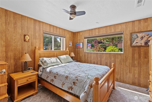 carpeted bedroom featuring ceiling fan and wood walls