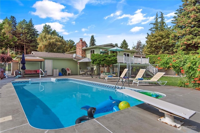 view of swimming pool with a patio area, a wooden deck, and a diving board