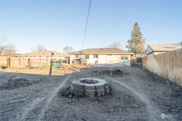 back of house featuring a trampoline, a fire pit, and a playground