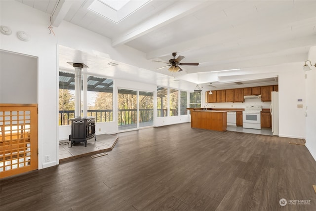 unfurnished living room with dark wood-type flooring, ceiling fan, a skylight, beamed ceiling, and a wood stove