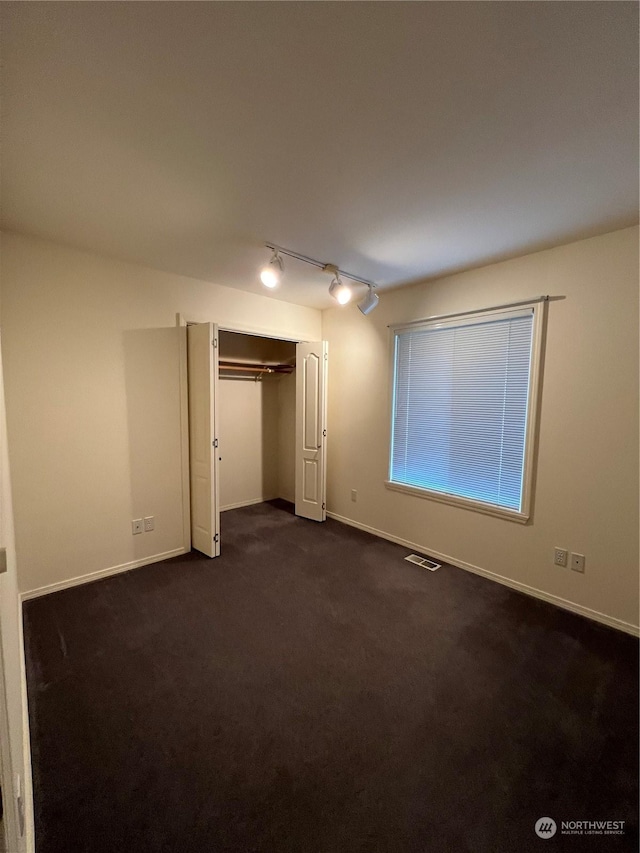 unfurnished bedroom featuring a closet, dark carpet, and rail lighting