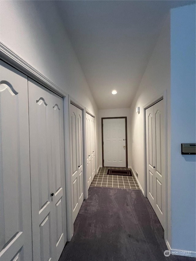 corridor with dark carpet and vaulted ceiling