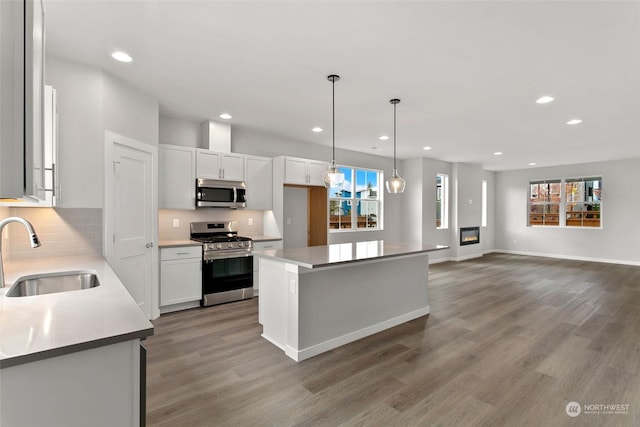 kitchen with pendant lighting, a kitchen island, sink, stainless steel appliances, and white cabinets