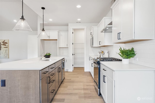 kitchen featuring appliances with stainless steel finishes, white cabinets, decorative light fixtures, sink, and an island with sink