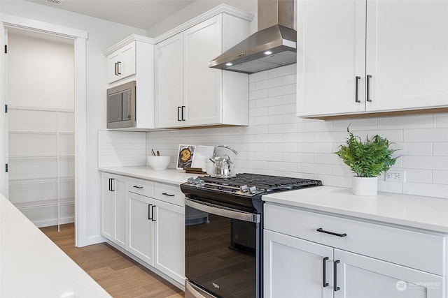 kitchen with wall chimney exhaust hood, backsplash, white cabinetry, light hardwood / wood-style floors, and stainless steel appliances