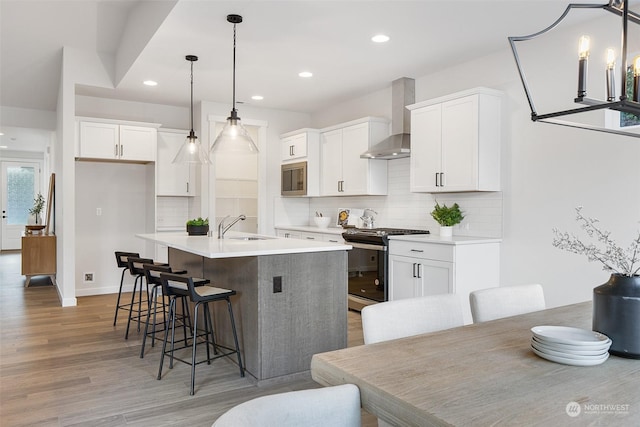 kitchen with white cabinetry, a kitchen island with sink, wall chimney range hood, decorative light fixtures, and stainless steel appliances