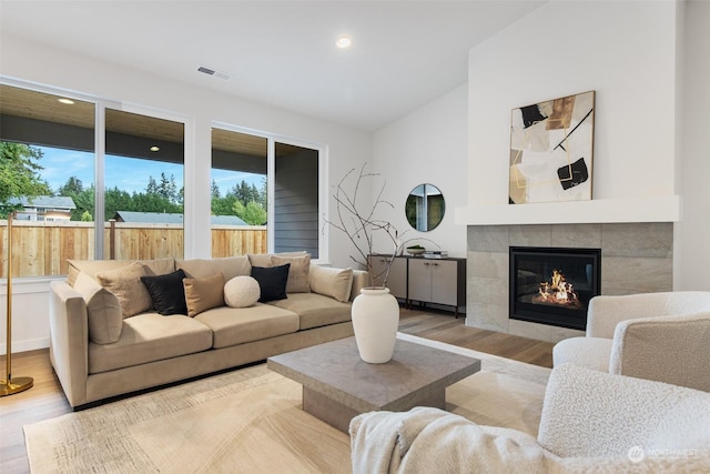 living room with light wood-type flooring, vaulted ceiling, and a tile fireplace