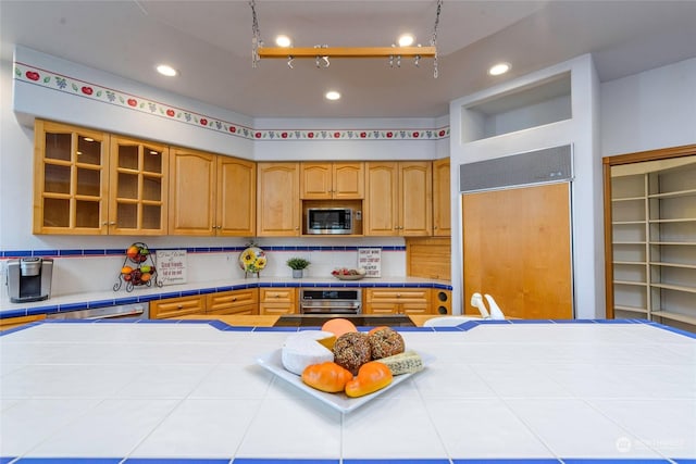 kitchen with built in appliances, tile countertops, and tasteful backsplash