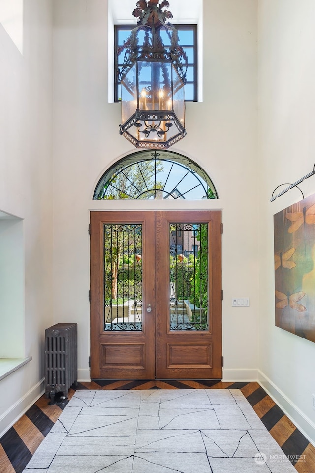 entryway featuring radiator, a towering ceiling, a notable chandelier, light hardwood / wood-style floors, and french doors