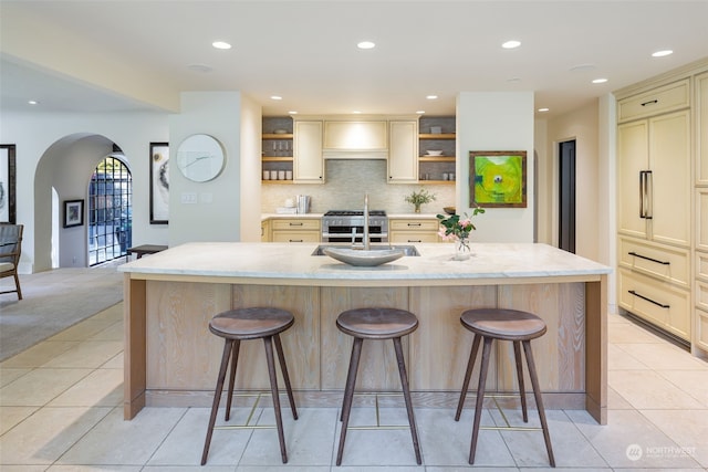 kitchen featuring an island with sink, sink, light stone counters, and a kitchen bar