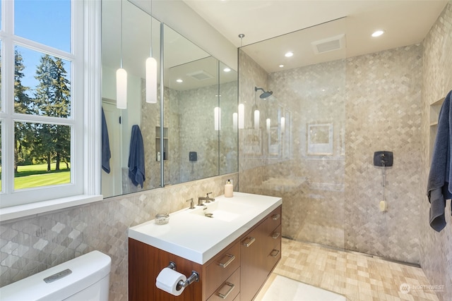 bathroom featuring a tile shower, a healthy amount of sunlight, tile walls, and toilet