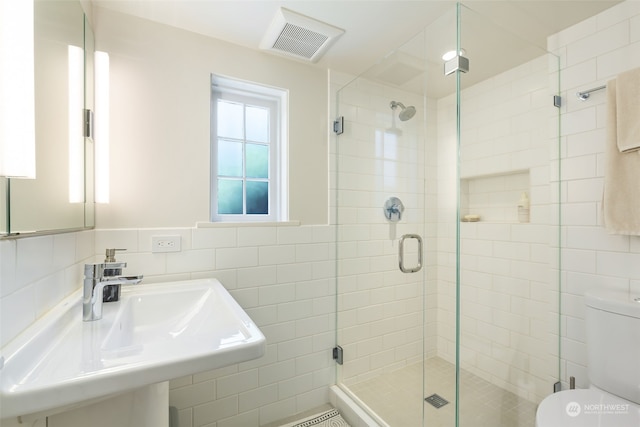 bathroom with toilet, sink, tasteful backsplash, tile walls, and a shower with door