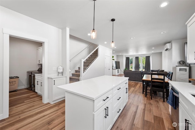 kitchen with hanging light fixtures, white cabinets, an AC wall unit, and light hardwood / wood-style floors