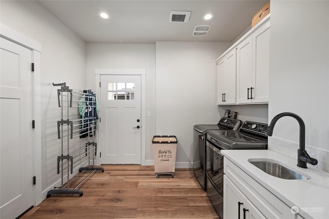 laundry room featuring cabinets, light hardwood / wood-style flooring, washing machine and clothes dryer, and sink