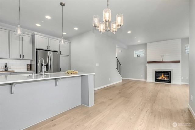 kitchen with stainless steel refrigerator with ice dispenser, hanging light fixtures, light wood-type flooring, tasteful backsplash, and a breakfast bar area