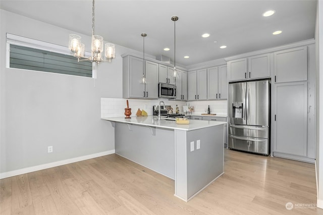 kitchen with decorative light fixtures, stainless steel appliances, decorative backsplash, kitchen peninsula, and light hardwood / wood-style flooring