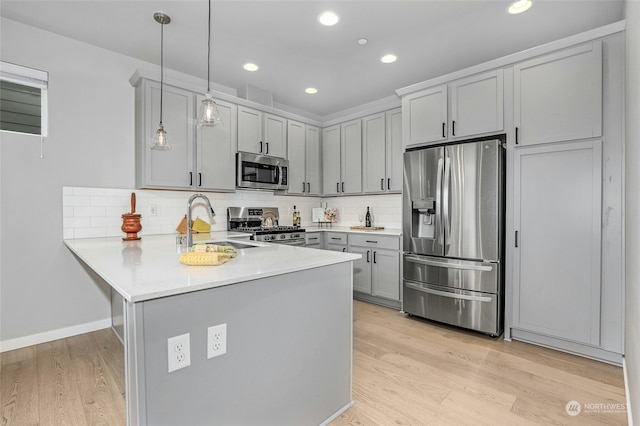 kitchen with appliances with stainless steel finishes, sink, hanging light fixtures, kitchen peninsula, and light wood-type flooring