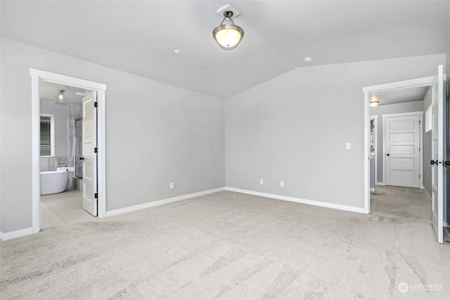 unfurnished bedroom featuring light colored carpet, vaulted ceiling, and ensuite bathroom