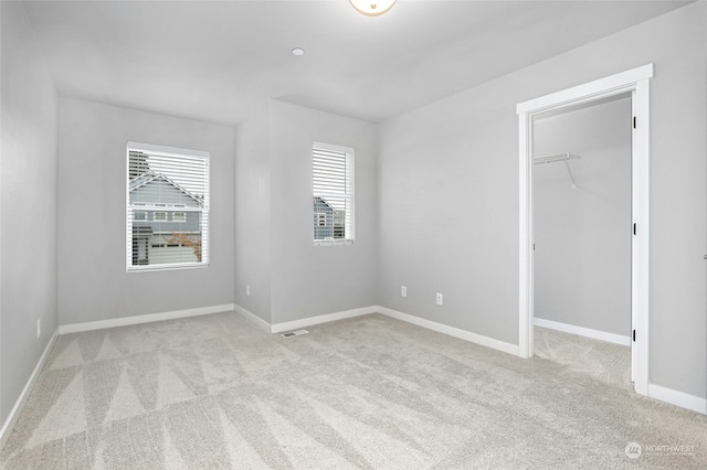 unfurnished bedroom featuring light colored carpet, a closet, and a spacious closet