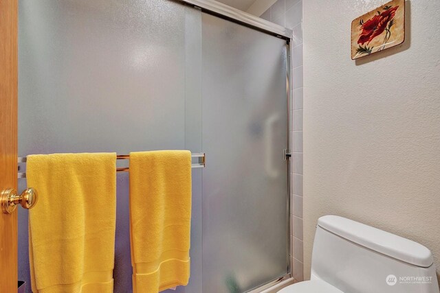 bathroom with a shower with shower door, a textured wall, and toilet