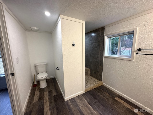 bathroom with hardwood / wood-style flooring, a tile shower, a textured ceiling, and toilet