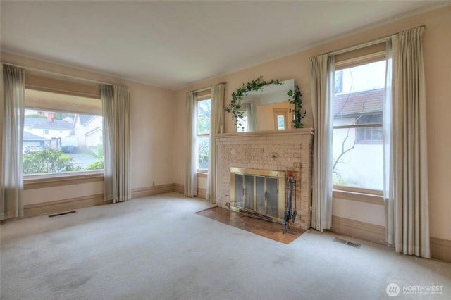 unfurnished living room with visible vents, baseboards, a fireplace, crown molding, and carpet flooring