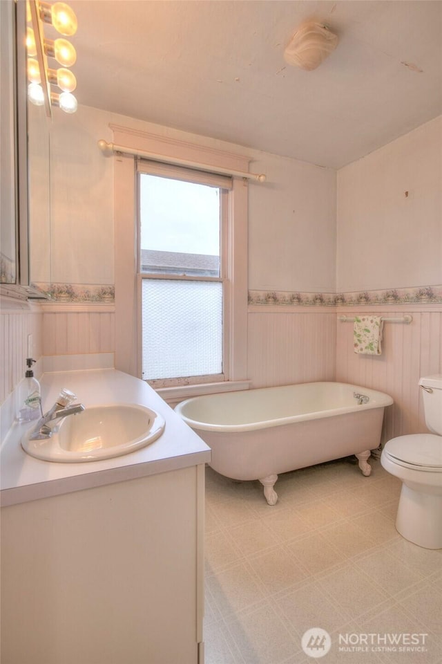 bathroom with a wainscoted wall, toilet, a freestanding tub, tile patterned floors, and vanity