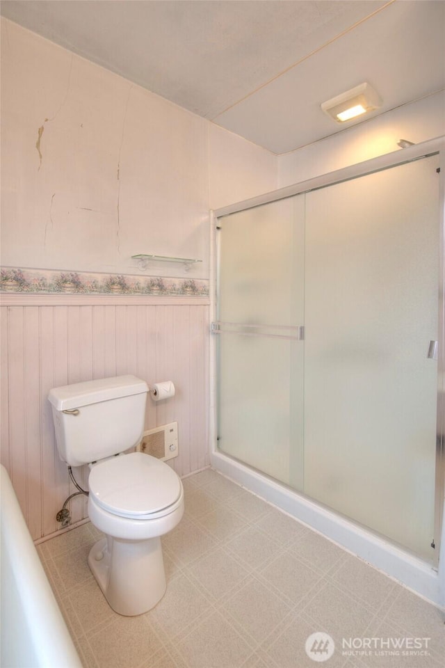 bathroom with toilet, a stall shower, and wainscoting