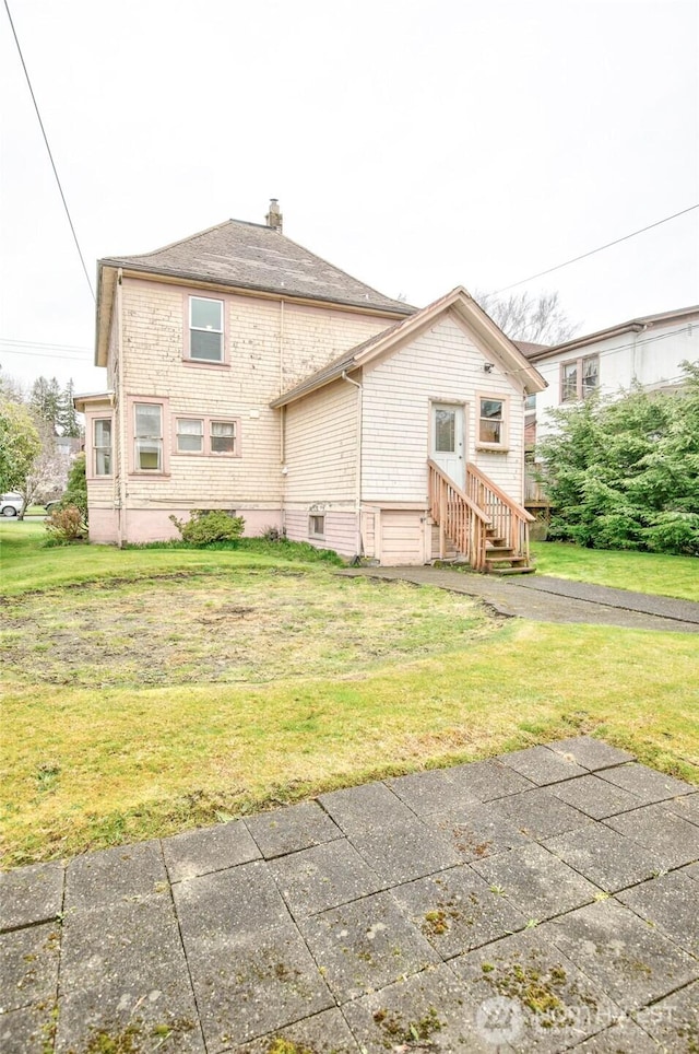 back of property featuring entry steps, a chimney, and a yard