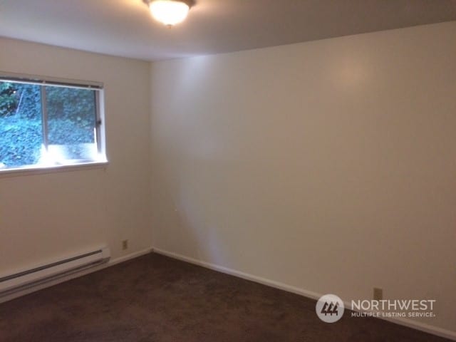 carpeted spare room featuring a baseboard heating unit