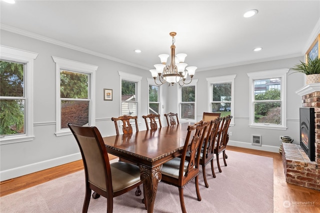 dining area with a fireplace, a notable chandelier, ornamental molding, and light hardwood / wood-style floors