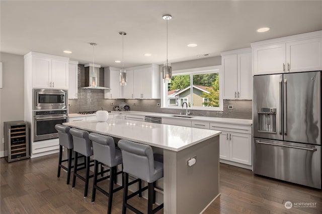 kitchen featuring white cabinets, a center island, wall chimney range hood, stainless steel appliances, and sink