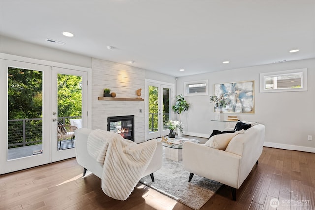 living area with wood-type flooring, a large fireplace, french doors, baseboards, and visible vents
