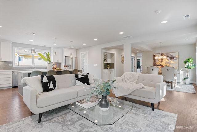 living area with visible vents, recessed lighting, hardwood / wood-style flooring, and an inviting chandelier