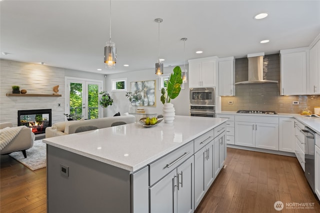 kitchen with dark wood-style flooring, appliances with stainless steel finishes, wall chimney exhaust hood, and a center island