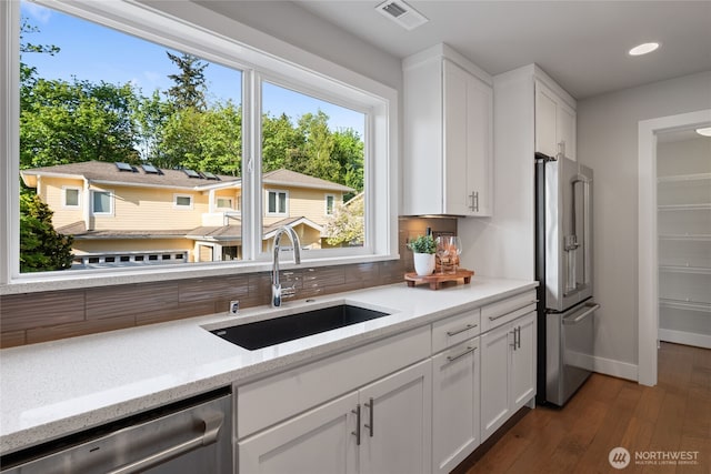 kitchen with white cabinets, a sink, stainless steel appliances, baseboards, and visible vents