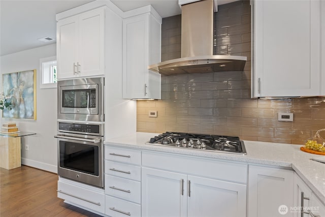 kitchen featuring white cabinetry, appliances with stainless steel finishes, decorative backsplash, and wall chimney exhaust hood