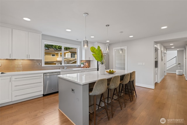 kitchen with stainless steel dishwasher, a kitchen breakfast bar, a center island, white cabinets, and backsplash