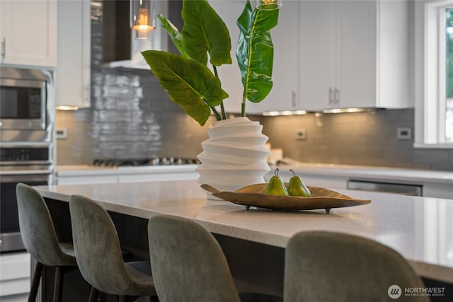 kitchen with appliances with stainless steel finishes, tasteful backsplash, white cabinetry, and a wealth of natural light