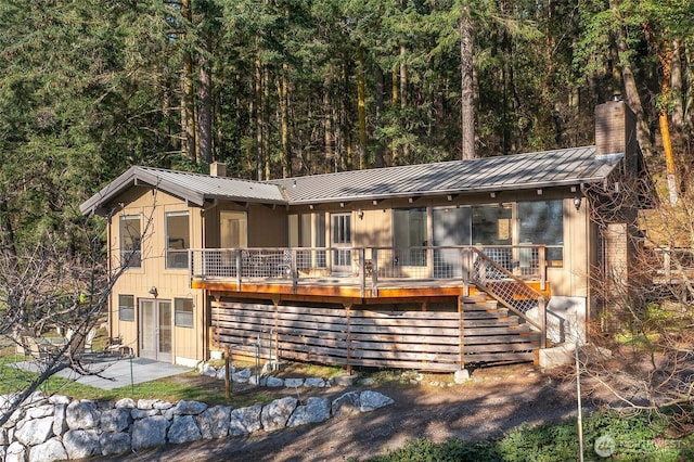view of front of home with stairway, a standing seam roof, a chimney, a patio area, and metal roof
