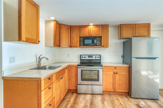 kitchen featuring brown cabinets, a sink, light wood-style floors, appliances with stainless steel finishes, and light countertops