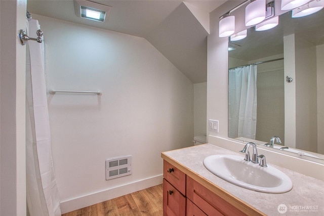 bathroom featuring visible vents, wood finished floors, baseboards, vanity, and vaulted ceiling