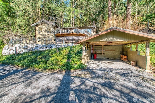 view of front of home featuring driveway, an exterior structure, an outdoor structure, a wooded view, and an attached carport